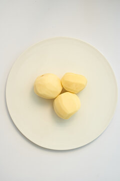 tep 4: Three peeled potatoes in a round ceramic bowl on a clean white background with copy space