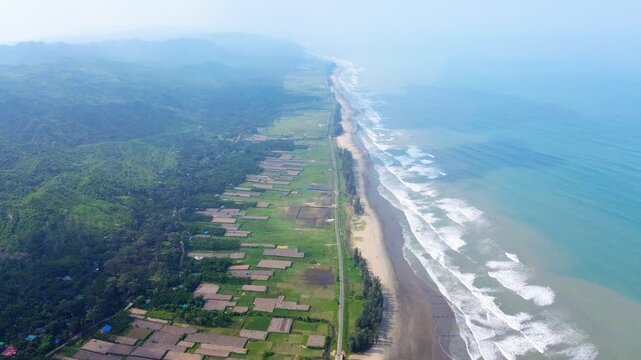 Aerial view of the endless sandy coastline with waves crashing on the shore and lush green hills in the background at Cox's Bazar, Chittagong Division, Bangladesh.
