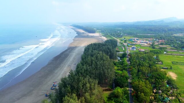Aerial view of the expansive sandy beach of Cox's Bazar with crashing waves, dense pine forest, and a coastal road under clear sky in Cox's Bazar, Chittagong Division, Bangladesh.