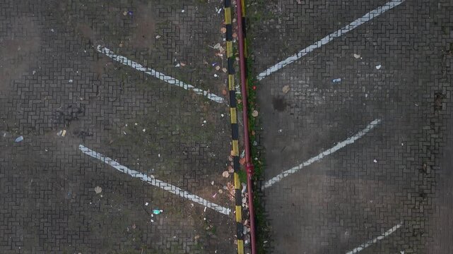 Top down aerial drone view of paving block parking lot with white parking lines and yellow black road divider. 