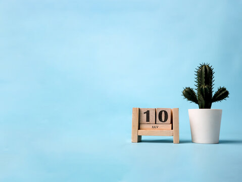 A wooden block calendar for July tenth with a plastic cactus plant on the side. Simple and clean design on a soft blue background.