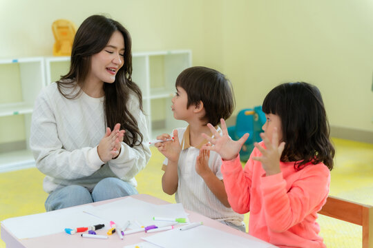 Happy kindergarten children and teacher playing a hand clapping game together in classroom