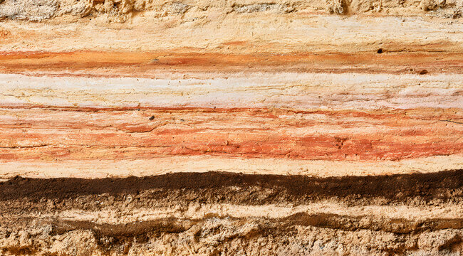 A background featuring a layered rammed earth wall texture with an abstract pattern made from natural clay, sand, and soil. The colors include beige, orange, and brown, stripes that add an organic tou