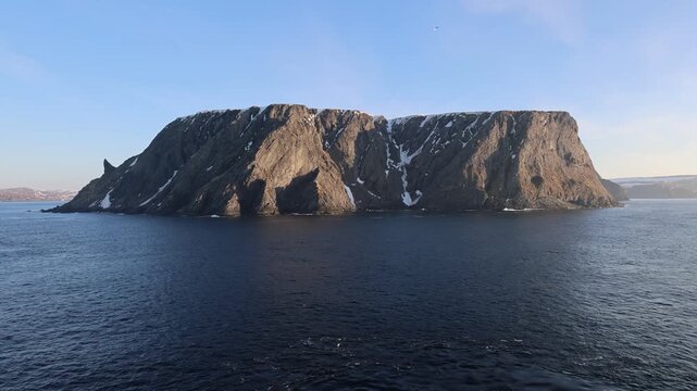 Aerial view of the North Cape plateau with steep rocky cliffs and patches of snow rising above the dark blue waters of the Barents Sea Nordkapp Municipality, Finnmark, Norway.