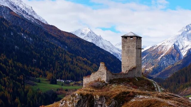 Aerial view of Ardez Castle ruins on a hill overlooking the valley with snow-capped mountains and blue sky in Scuol, Grisons, Switzerland.