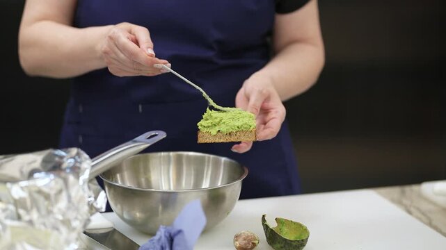 The chef at the master class spreads mashed avocado on bread. Very soft focus