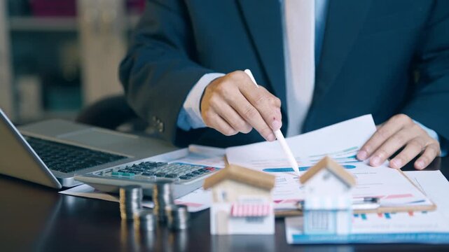 Businessman analyzing financial charts, counting coins, and using a calculator to evaluate asset sales and profits.