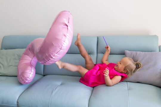 Toddler Playing With Inflatable Balloon On Living Room Sofa