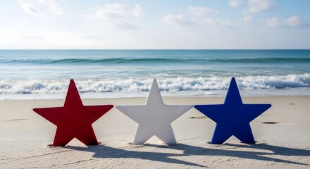 Labor Day Three decorative stars in red white and blue colors sitting on a pristine sandy beach with rolling ocean waves in the background