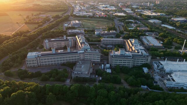 Aerial view of the GSK Stevenage pharmaceutical research and development site during golden hour with lush greenery in Stevenage, England, United Kingdom.