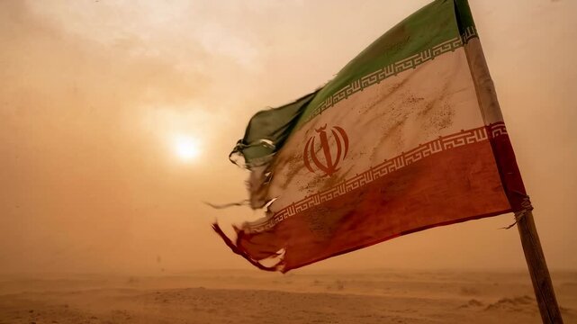 Iranian flag flutters with torn edges. Hazy sky surrounds the setting sun. Dust covers the desert landscape. Resilience. Good for cultural themes. Ideal for environmental projects