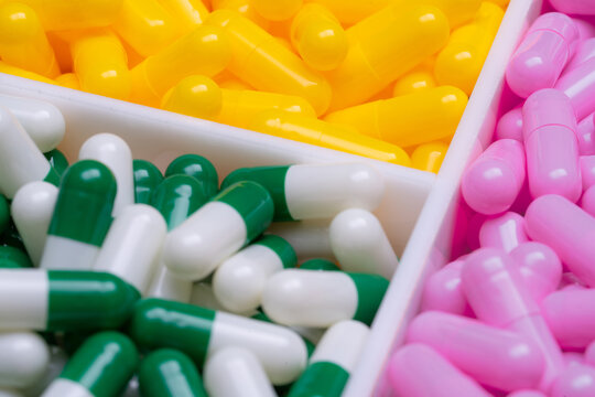 Selective focus on capsule pills in plastic box. Pharmaceutical industry. Pink, yellow, and green-white capsule pills. Vitamins and supplements concept. Bright colors capsule in tray. Healthcare.