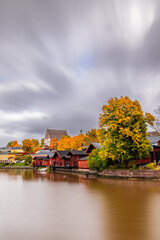 Fototapeta premium Scenic autumn view of Old Porvoo, Finland, featuring colorful traditional wooden houses and the Porvoo Cathedral overlooking the river, framed by golden reeds in the foreground.