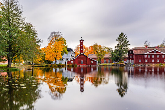 Historic red wooden buildings and fire station tower of Str&ouml;mfors Ironworks in Loviisa, Finland, perfectly reflecting on the calm river surface amidst colorful autumn foliage.