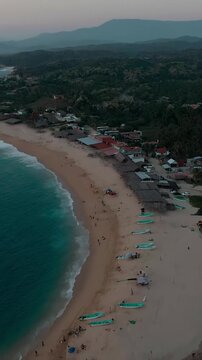 Vertical drone flyover along El Faro beach showcasing fishing boats, tourists, waves crashing on the beach and camping bower spots in Faro de Buceria, Michoacan, Mexico.