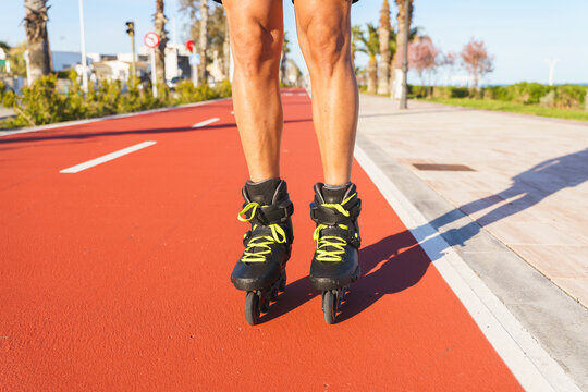 Man's legs in inline skates moving along a red path near the beach