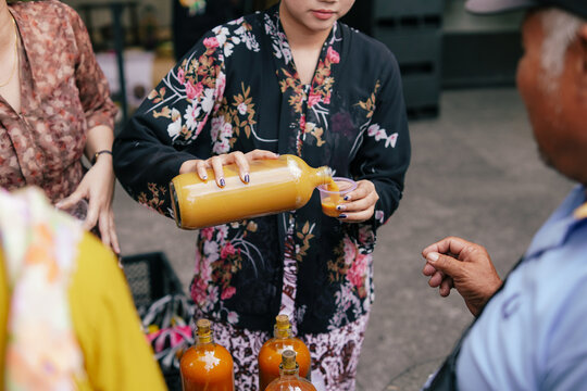 Woman in traditional kebaya serving jamu herbal drink at an outdoor market, celebrating Indonesian culture, local traditions, herbal wellness, and authentic street commerce