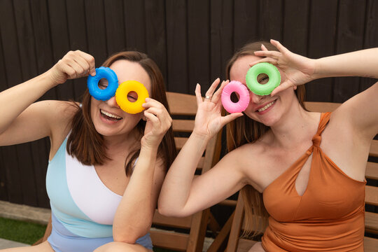 Two cheerful women in swimsuits holding small colorful swim ring