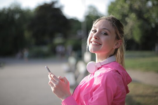Happy young woman with headphones using phone outdoors
