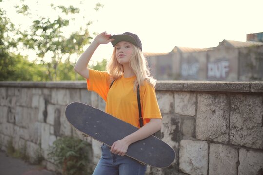 Young skater woman poses with her board at sunset