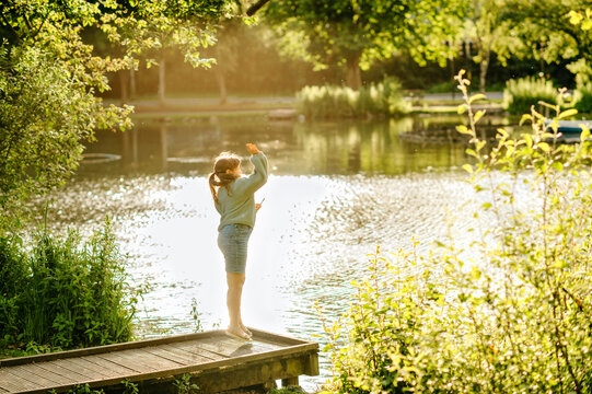 School age girl standing on wooden dock beside sunlit lake in summer