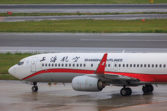 Fukuoka, Fukuoka Japan - 2025 May 24: Close-up of a Shanghai Airlines Boeing 737-800 showing the forward fuselage and engine as it taxis at Fukuoka Airport in the rain.