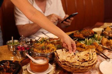 Fototapeta na wymiar Diner Reaching for Naan Bread at Traditional Indian Restaurant Table