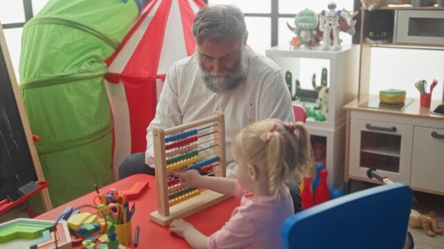 Man guides girl moving beads on wooden abacus at red table in playroom inside building; calm learning bonding.