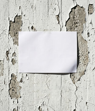 Blank white paper note taped on rustic peeling paint wall, copy space mockup, grunge texture background