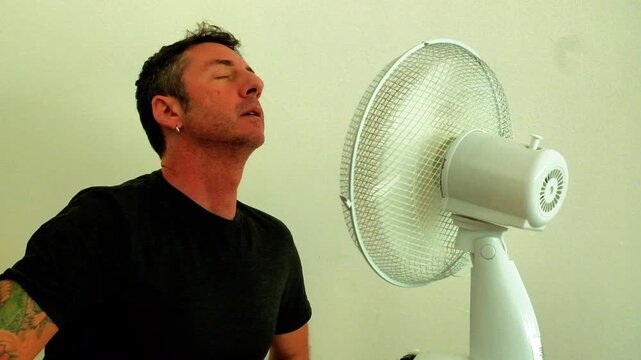 A man enjoys the coolness of the fan up close to counteract the summer heat. The man in the video is forty-two years old, is an Italian of Caucasian origin and wears a dark gray T-shirt