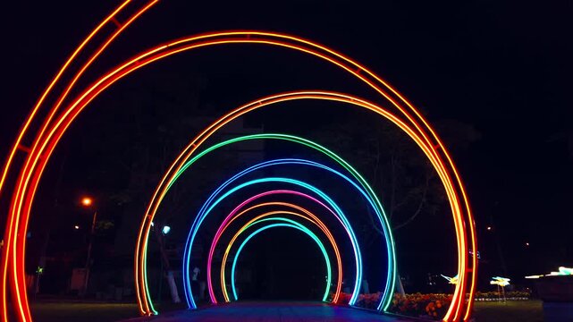 colourful neon light tunnel with glowing rainbow arches and futuristic night perspective, illuminated LED walkway with vibrant festive decoration and abstract cyberpunk background 4k