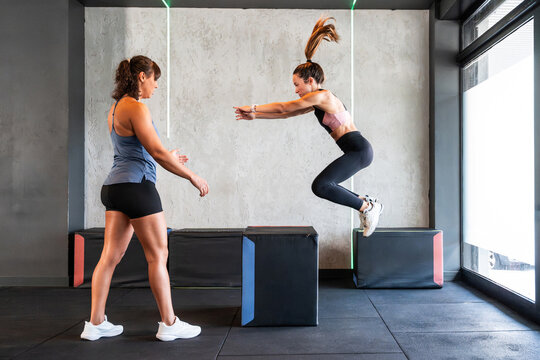 Woman doing box jump in gym with coach during training