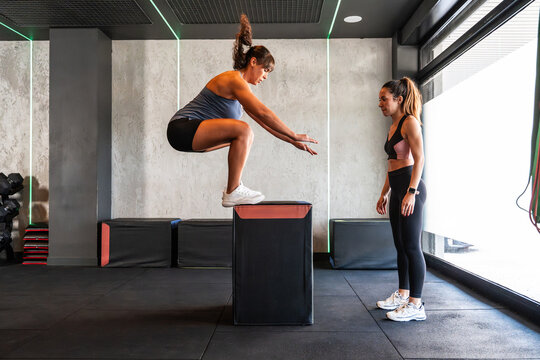 Woman performing box jump in gym with personal trainer