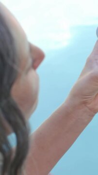 Vertical video: Lifting woman in swimsuit showing glass with lemon, strawberry, revealing pool sky