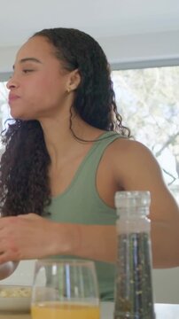 Vertical video: Leaning, woman in green top having meal at home counter with juice and pepper mill