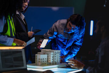 Construction team with South Asian male and diverse members reviews architectural plans and scale...