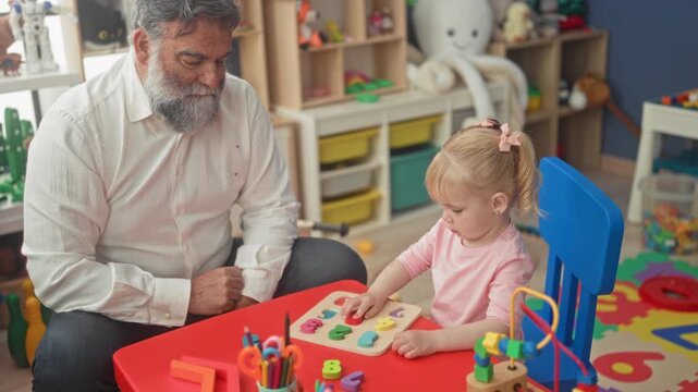 Man sits beside little girl guiding her hand to place wooden number puzzle pieces on a red table in a building playroom for preschool activity; tender learning.