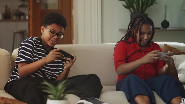 Happy Black siblings communicating while playing video games on their phones