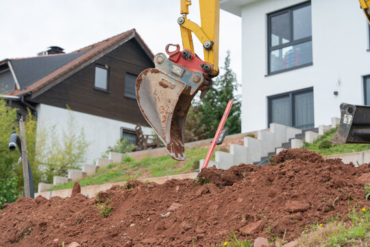 Mini excavator working in front of modern house. Residential backyard landscaping and earthworks.