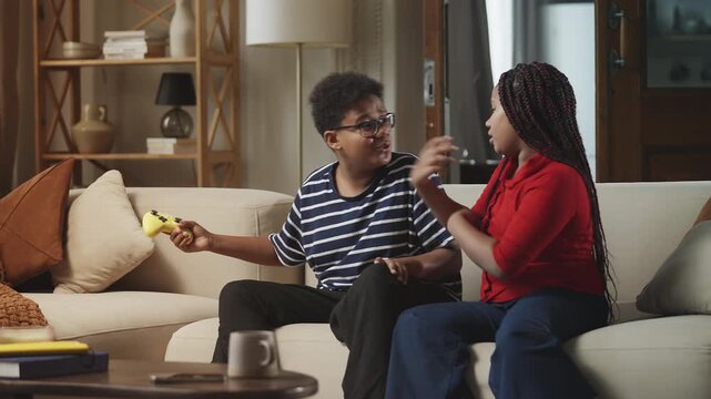 Sister playfully taking a gamepad from her brother while gaming at home