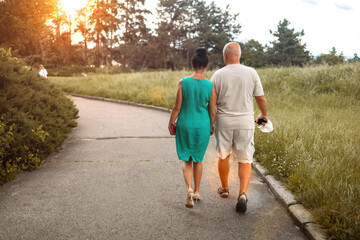 Obraz premium Elderly, happy couple and holding hands in park for bonding, fresh air or outdoor walk together. Back view senior man and woman on path or trail for holiday, weekend or retirement in nature or woods.