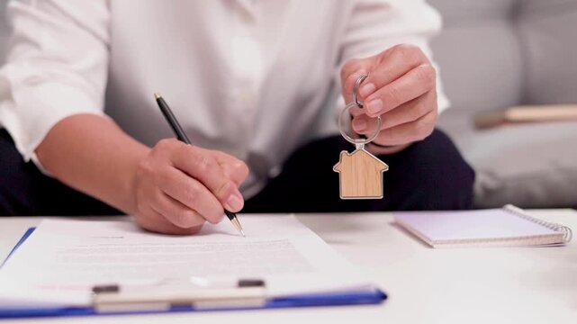 Person signing documents and holding a house key on a table with a notebook
