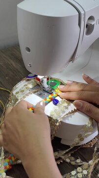 Close-up of hands operating a sewing machine to stitch decorative trims and handcrafted embellishments onto fabric, showcasing garment making, textile craftsmanship, and fashion design.