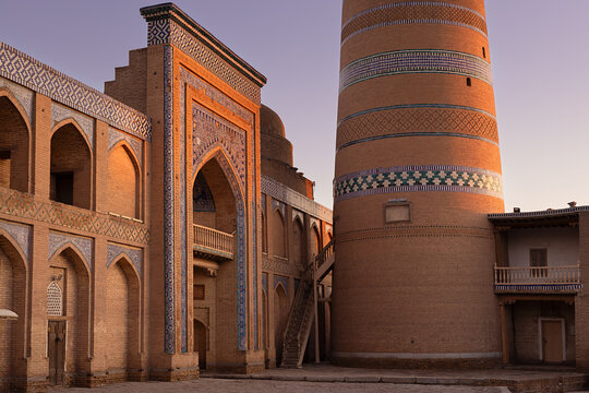 Islam Khoja Minaret and madrasah in Khiva at twilight with ornate tilework and brick facades. Historic Ichan Kala architecture ideal for travel publications and cultural heritage projects.