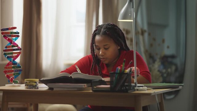 Focused African American girl studying at home, writing homework in a notebook