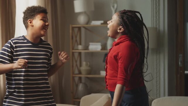 Carefree Black teen boy and his sister dancing and singing at a home party