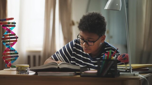 Diligent African American boy in eyeglasses doing homework in a noisy room