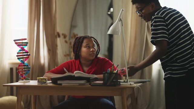Brother teasing his younger sister for being diligent and doing homework