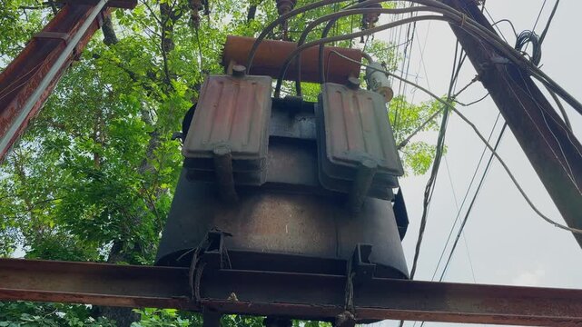 Camera orbiting around a pole mounted electrical distribution transformer, capturing power cables, insulators and utility infrastructure framed by surrounding trees and daylight sky.