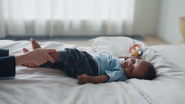 Professional masseuse or mother doing baby massage for infant, healthcare. Childhood and parenthood, joyful african american infant relaxing in bed, treatments for save body and development muscles